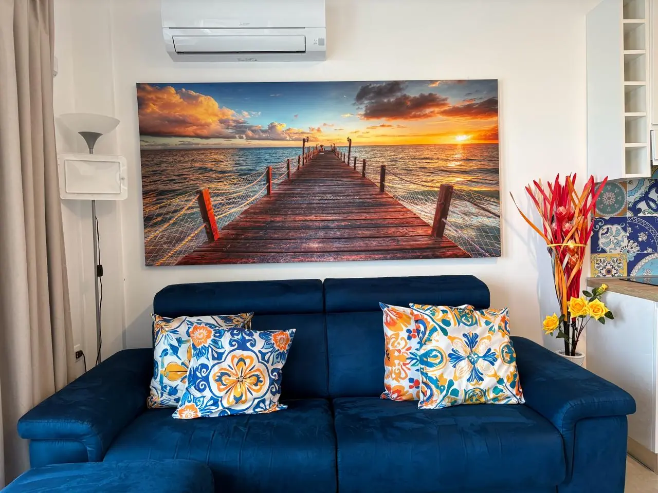 Casa di Rita — soggiorno con divano blu e quadro del pontile al tramonto